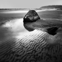 Ein großer Felsen, der an einem Sandstrand nahe des Wassers liegt. 