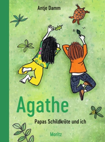 Zwei Kinder liegen auf einer Wiese und locken eine Schildkröte mit Laubblättern an.