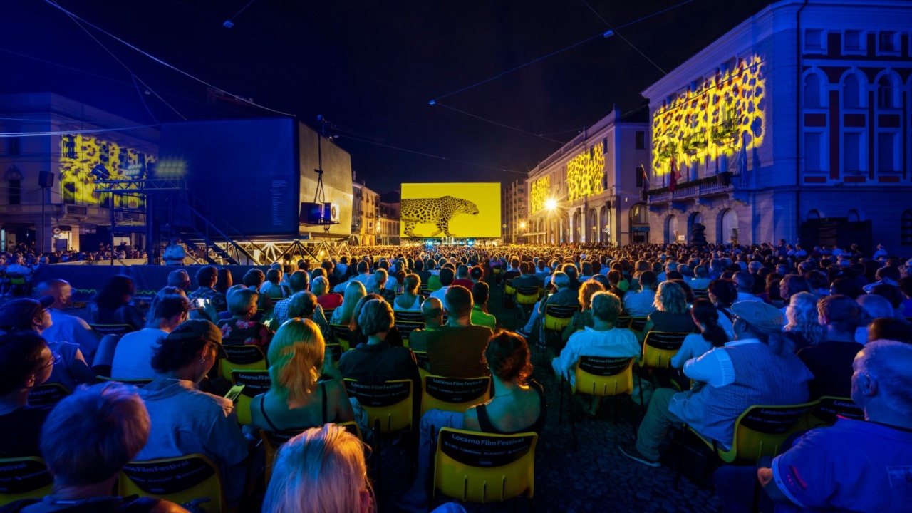 Eine große Filmeleinwand, davor Zuschauer, die auf Stühlen sitzen und auf die Leinwand blicken
