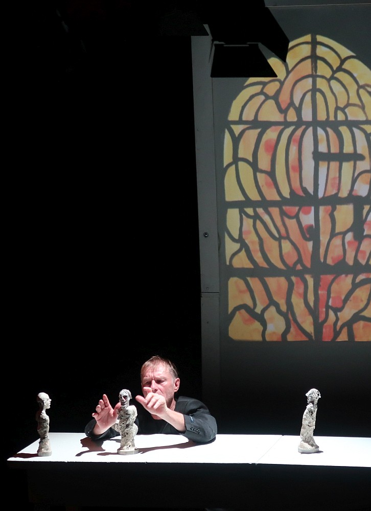 In einem dunklen Raum arrangiert ein Mann kleine menschliche Figuren auf einem beleuchteten Tisch