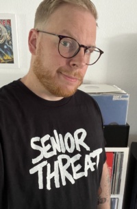 Porträtfoto eines Mannes mit Bart, Brille und schwarzem T-Shirt