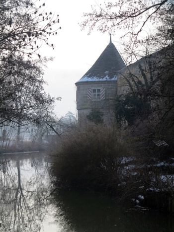 Ein Turm an einem kleinen Fluss. Daneben stehen kahle Bäume.