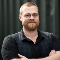 Porträtfoto eines Mannes mit Bart, Brille und schwarzem Poloshirt