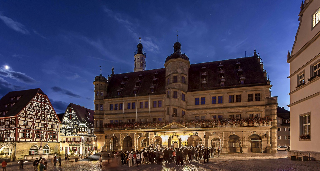 Ein großes altes Rathaus vor nächtlichem Himmel. Davor steht eine große Gruppe von Menchen