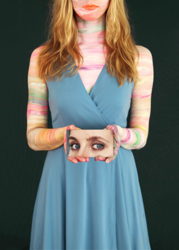 Eine Frau im blauen Kleid hält ein kleines Bild vor ihren Körper, das menschliche Augen zeigt.