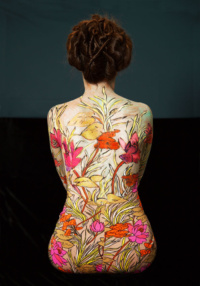Der Rücken einer sitzenden Frau. Darauf sind Blumen gemalt.