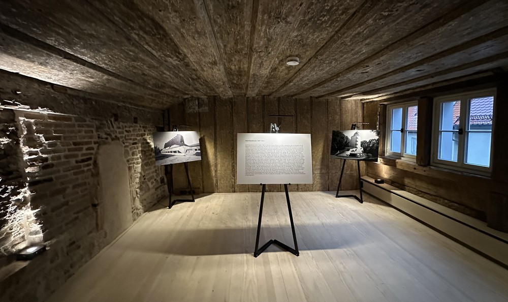 In einer alten leeren Wohnstube stehen großformatige Bilder und Texttafeln auf Holzständern 