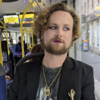 Eine Person mit Bart und Lippenstift, die in einem Bus sitzt.