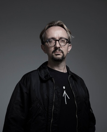 Ein Porträtfoto des Interviewteilnehmers mit schwarzer Jacke vor einem dunklen Hintergrund