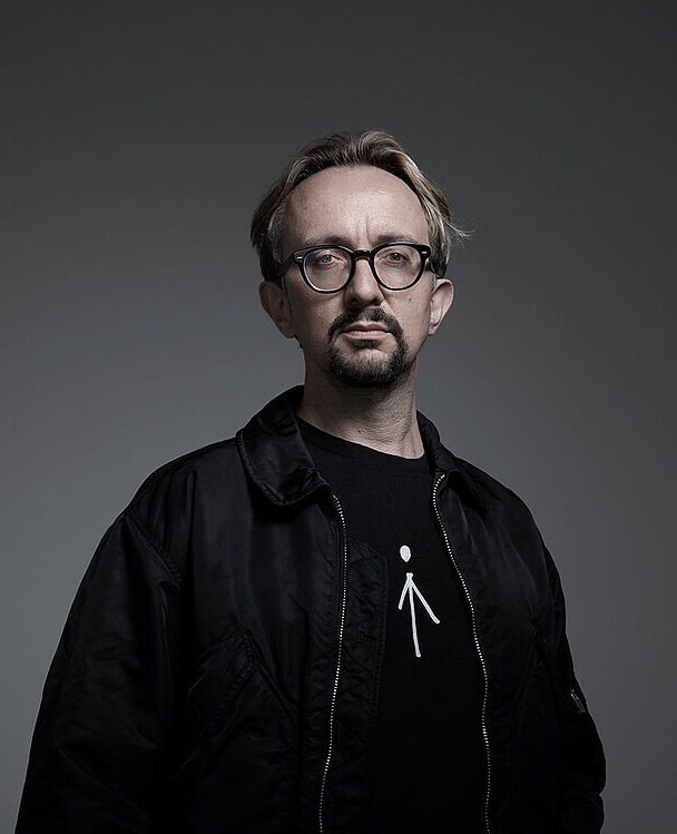 Ein Porträtfoto des Interviewteilnehmers mit schwarzer Jacke vor einem dunklen Hintergrund